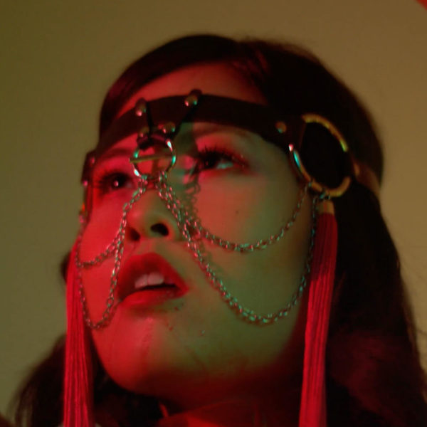 Artist Lena Chen wears decorative headgear made with leather and chains in a photo studio setting.