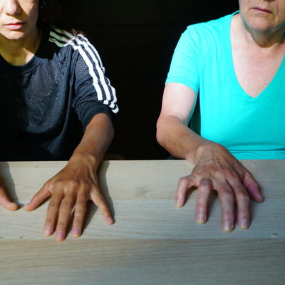 Two individuals sit side by side with both of their hands spread out on a table.