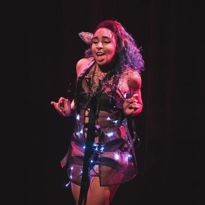 Rye wears a sheer dress adorned with fairy lights and black heeled boots on stage.
