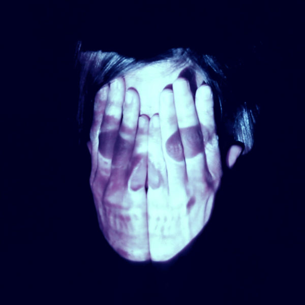 A person covering their face with both hands while and image of a skull projects on top.